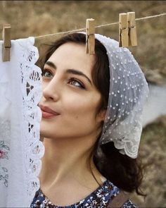 a woman wearing a veil and looking up at clothes hanging on a line with clothes pins in front of her head