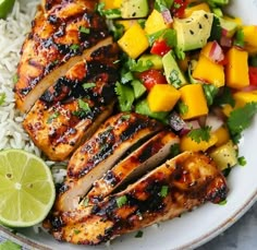 grilled chicken with mango salsa and rice on a white plate next to lime wedges