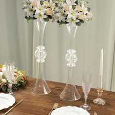 two tall vases filled with white flowers on top of a wooden table next to candles