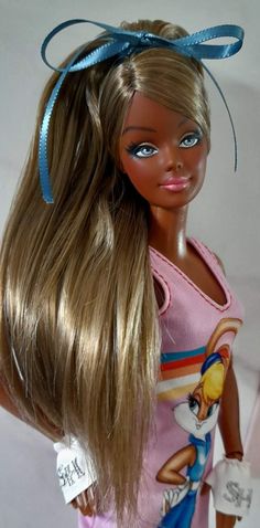 a barbie doll with long blonde hair wearing a pink shirt and blue ribbon around her head