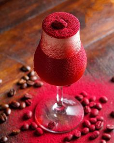 a red drink sitting on top of a table next to coffee beans