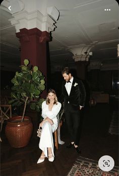 a man in a tuxedo standing next to a woman sitting on a chair