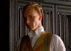 a young man wearing a vest and bow tie standing in front of a wooden paneled wall