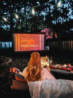 a woman sitting in a chair watching a movie on the big screen outside at night