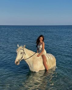 a woman riding on the back of a white horse in the middle of the ocean