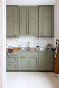 an open kitchen with green cabinets and white tile backsplash, along with wood flooring