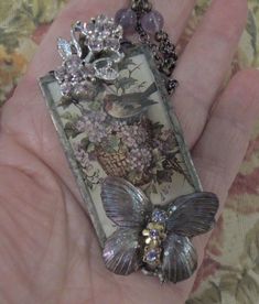 a person is holding a butterfly necklace in their hand with flowers and butterflies on it