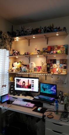 two computer monitors sitting on top of a desk in front of shelves filled with toys