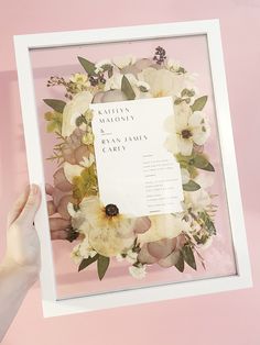 a person holding up a white frame with flowers on it