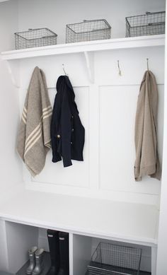 two coats hanging on the wall next to some shoes and baskets in a room with white walls