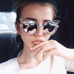 a woman wearing sunglasses sitting in the back seat of a car with her hand on her chin