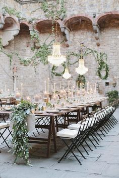 a long table set up with white chairs and greenery on the wall behind it