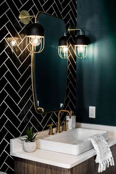 a bathroom vanity with two mirrors and lights on it's sides, in front of a black tiled wall