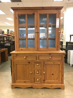 a wooden china cabinet with glass doors and drawers on display in a store or showroom