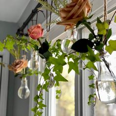 flowers are hanging from the window sill in front of glass vases filled with water and greenery