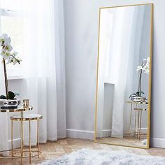 a large mirror sitting on top of a wooden floor next to a table with flowers