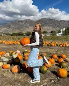 a girl standing in front of a field full of pumpkins with mountains in the background