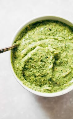 a white bowl filled with pesto sauce on top of a table next to a wooden spoon