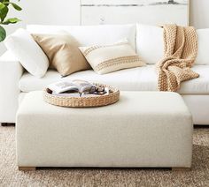 a living room with a white couch, ottoman and coffee table in front of it