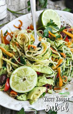 a white plate topped with zucchini noodles and veggies next to a lime wedge