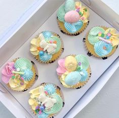 six cupcakes in a box decorated with pastel colors and bows on them