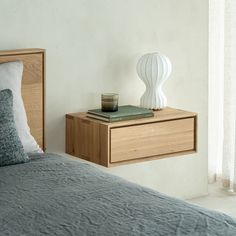 a nightstand with a book and candle on it next to a bed