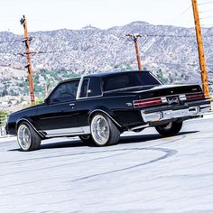 an old black car is parked on the side of the road in front of some telephone poles