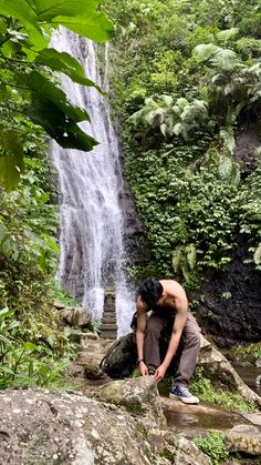 a man kneeling down in front of a waterfall