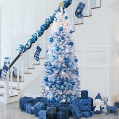 a blue and white christmas tree with presents under the bannister in front of it