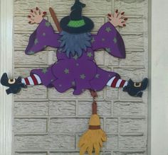 a purple witch door hanger hanging on the side of a white brick wall with a broom