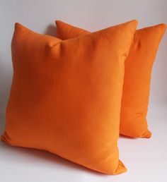 two orange pillows sitting next to each other on a white surface with the same color as the pillow