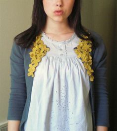 a woman standing in front of a wall wearing a white dress with yellow flowers on it