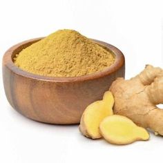 ginger root powder in a wooden bowl next to it's roots and sliced ginger