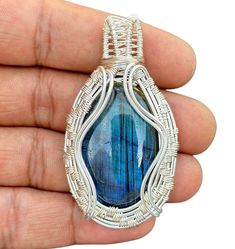 a hand holding a wire wrapped pendant with a blue glass stone in it's center