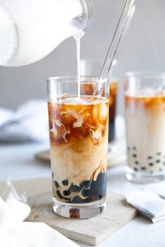 a pitcher pouring ice into a glass filled with iced coffee and liquid on top of a cutting board