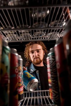 a man with long hair and beard standing in an open refrigerator holding a can of soda