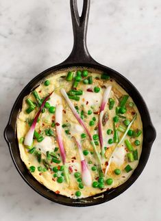 an omelet with peas and onions in a cast iron skillet on a marble surface