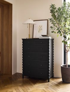 a black dresser sitting next to a potted plant on top of a hard wood floor