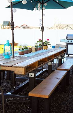 a picnic table with an umbrella over it and potted plants on the other side