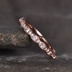 a rose gold wedding band with white diamonds on the inside and outside, sitting on top of a rock