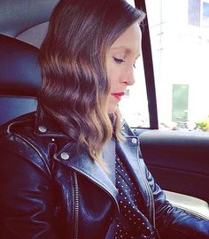 a woman sitting in the back seat of a car looking at her cell phone while wearing a leather jacket