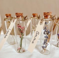 four glass bottles with flowers in them and tags attached to the top, on a white table cloth