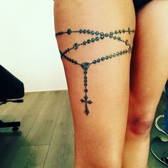 a woman's leg with a rosary tattoo on her left thigh, and a cross at the ankle