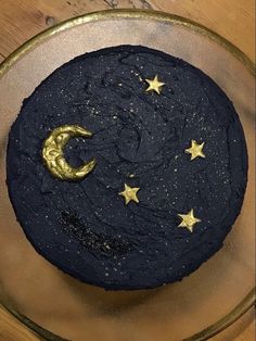 a black cake with gold stars and a crescent on top is sitting in a glass bowl