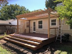 a house with a wooden deck in the yard next to a tree and ladders