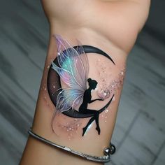 a woman's wrist tattoo with a fairy on the moon and a small tinkerbell