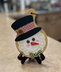 Snowman Cutting Board Decoration 4 1/2" wide by 6 1/2" tall Can be displayed on an easel or hung on the wall. (easel in picture not included) Paper doily makes the snowman's face...his top hat is laser cut and hand painted, buttons for the eyes, trim on hat, and nose, ribbon for bow tie and trim on hat. Sparkly glitter makes the snowman shine. Ginger Bread Crafts, Nursing Home Christmas, Angel Wings Flower, Wall Easel, Diy Snowflakes, Burlap Monogram, Xmas Projects, Kids Christmas Crafts, Snowman Craft