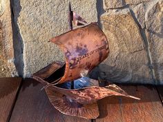 a metal boat is sitting on top of a wooden table next to a stone wall