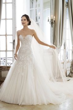 a woman in a wedding dress standing next to a window