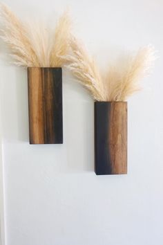 two wooden vases with dried grass in them on a white wall next to each other